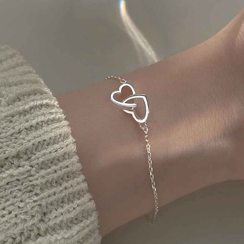 Silverpläterat armband på handled. Subtil och elegant design med två sammanlänkade hjärtan, idealiskt för daglig användning.