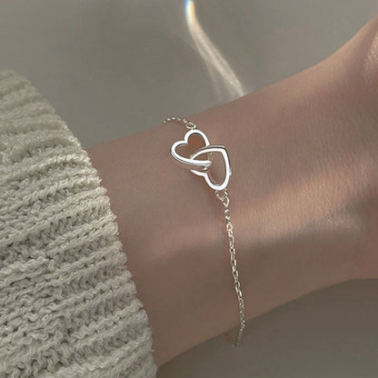 Silverpläterat armband på handled. Subtil och elegant design med två sammanlänkade hjärtan, idealiskt för daglig användning.